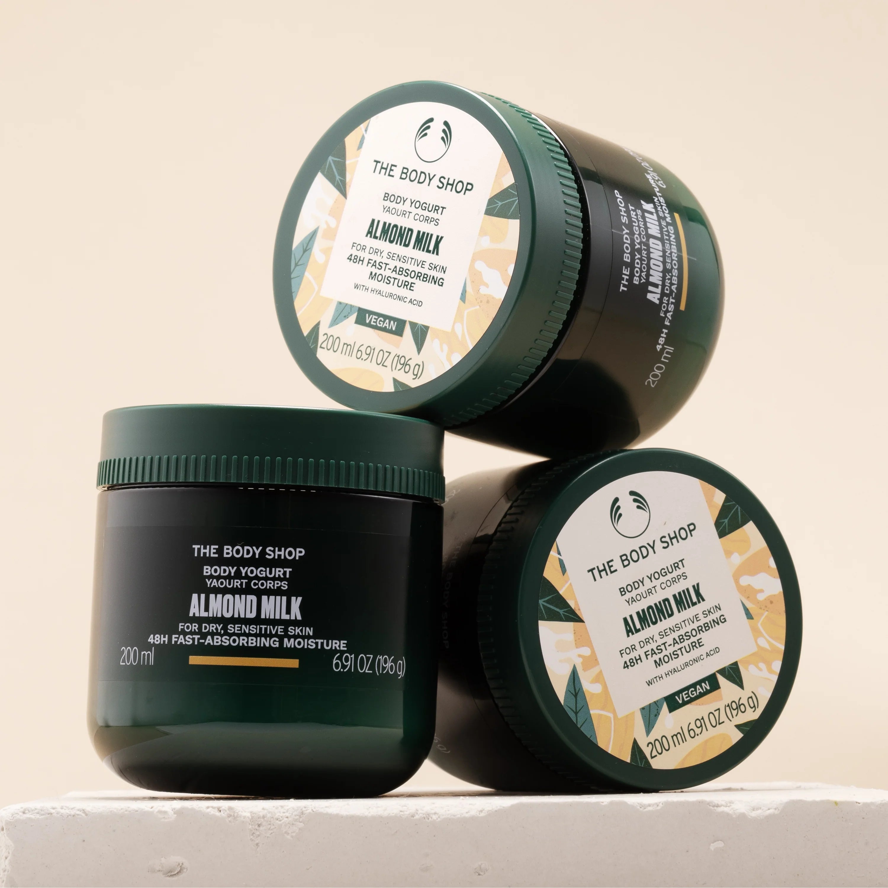 Three jars of The Body Shop Almond Milk Body Yogurt on a beige background