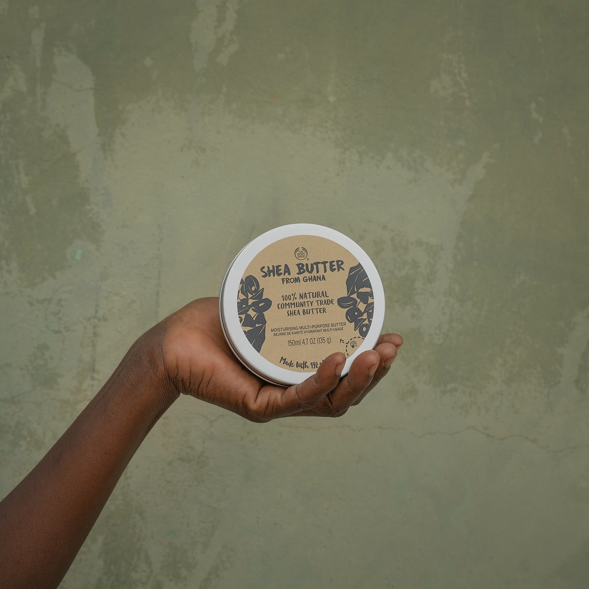 Hand holding a container of shea butter against a textured green background