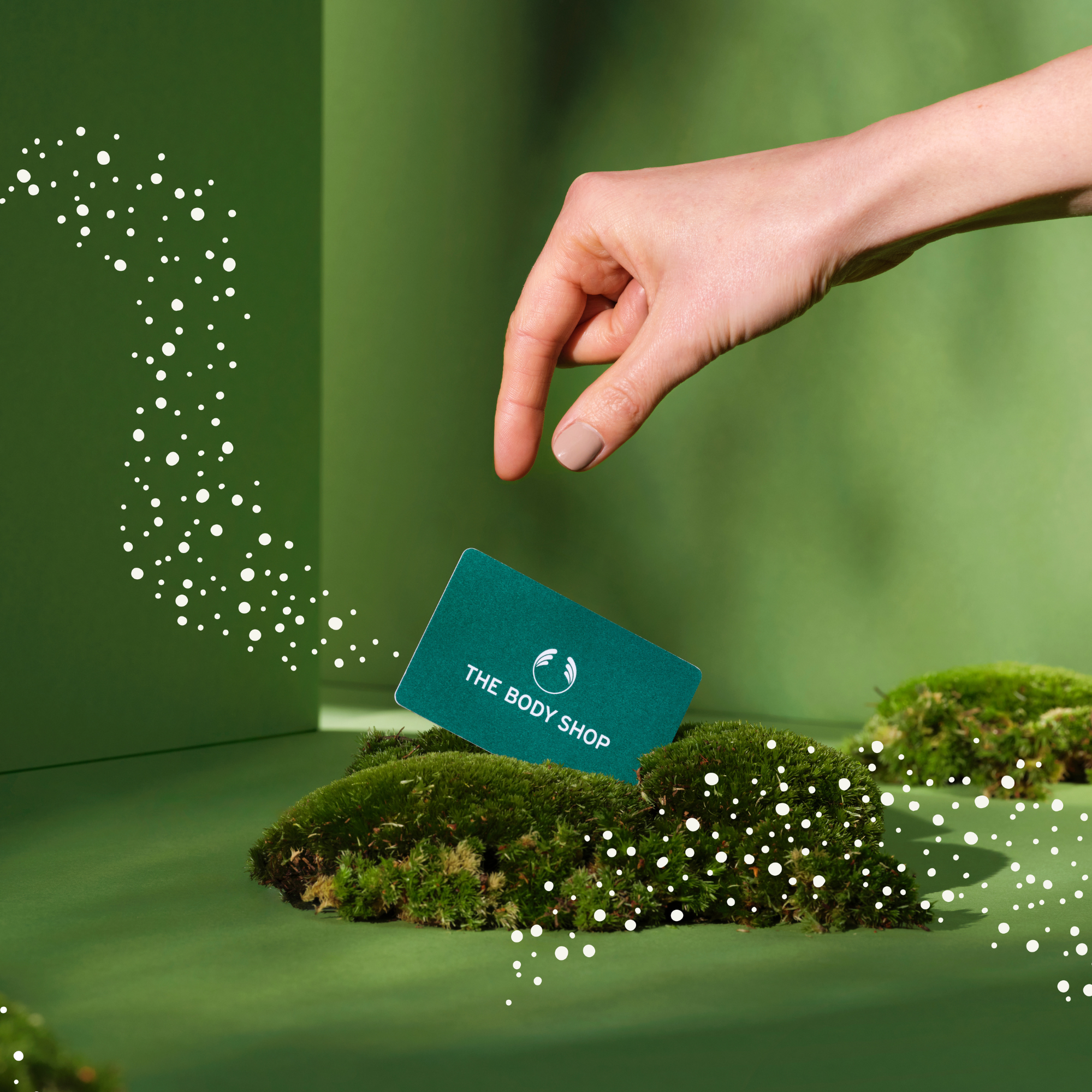 Hand holding a The Body Shop card with a green background and moss-like elements.
