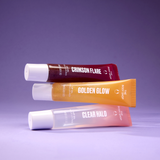 Three lip balm tubes from The Body Shop's 'The Lip Shop' are stacked diagonally on a purple background. The tubes are labeled 'CRIMSON FLARE' in dark red, 'GOLDEN GLOW' in orange, and 'CLEAR HALO' in translucent pink, all with white caps.