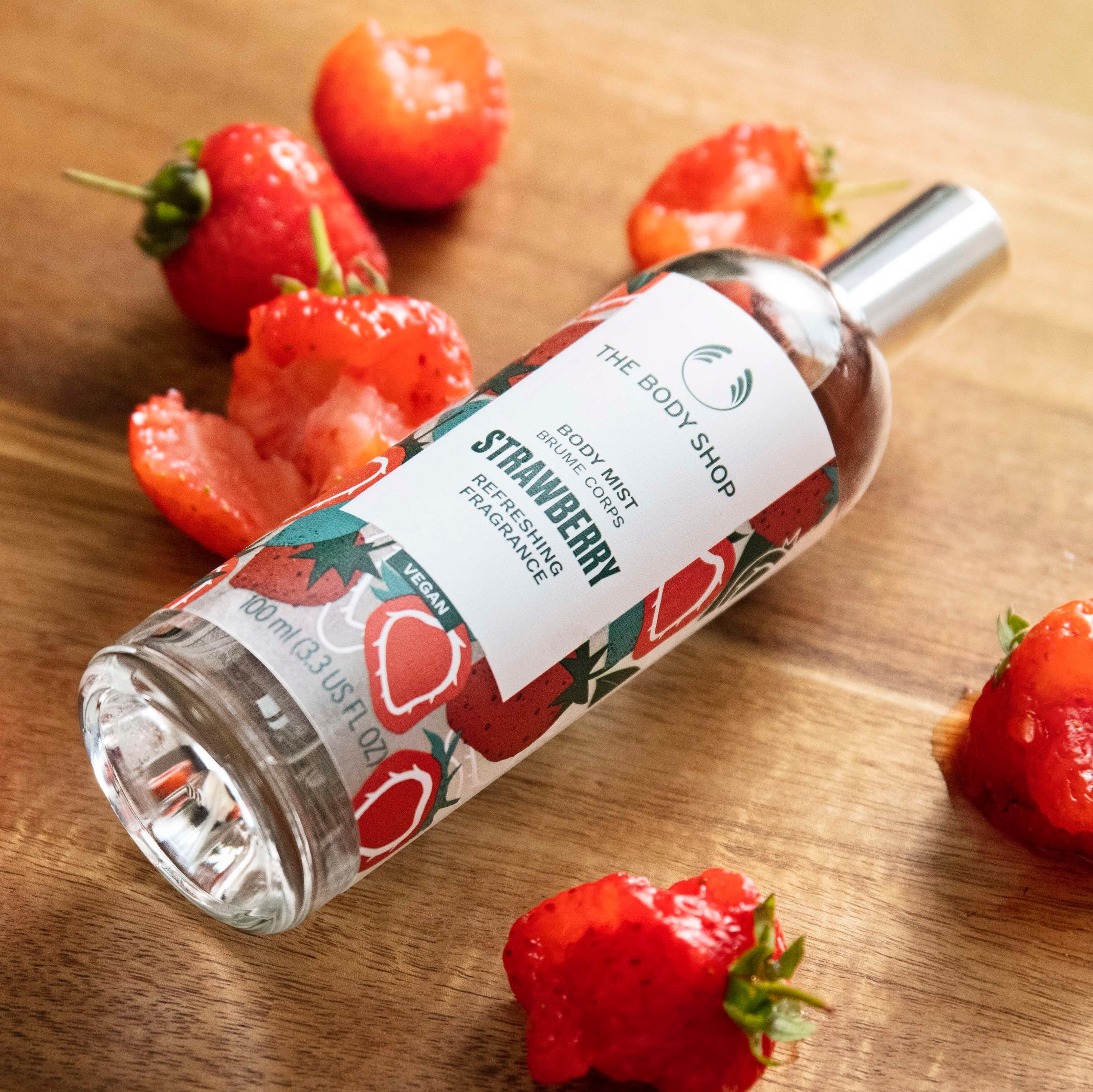 Strawberry-scented body mist bottle with strawberries on a wooden surface
