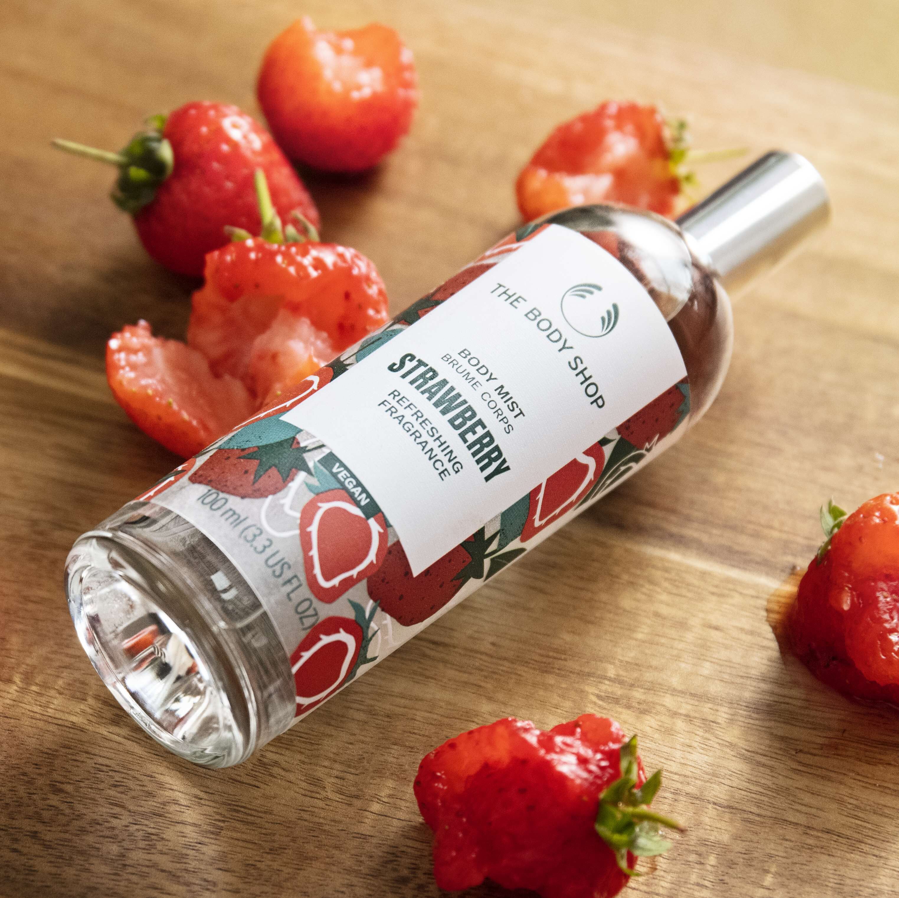 Strawberry-scented body mist bottle with strawberries on a wooden surface
