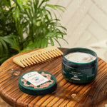 Shea butter product with a comb on a wooden board with plants in the background