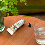 Tube of toothpaste with a glass of water and a plant on a wooden table