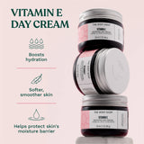 Stack of The Body Shop Vitamin E day cream jars with product benefits on a light pink background