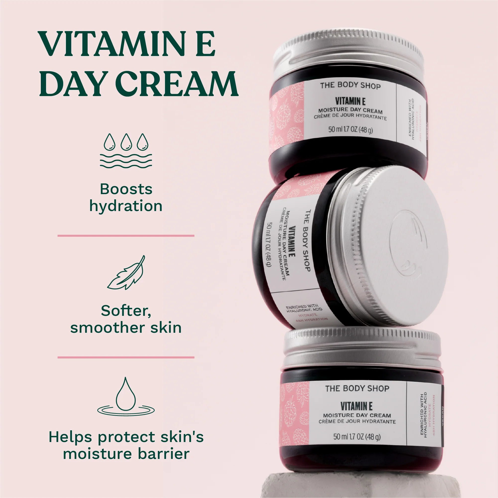 Stack of The Body Shop Vitamin E day cream jars with product benefits on a light pink background