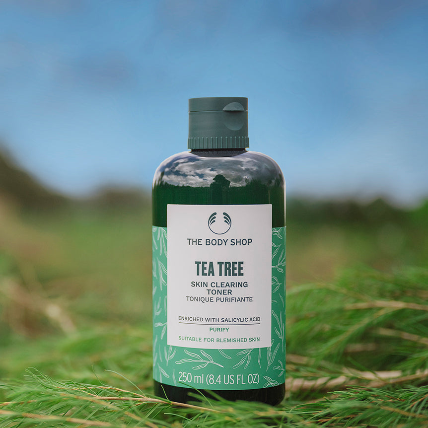 Bottle of The Body Shop Tea Tree Skin Clearing Toner on grass with a blurred natural background
