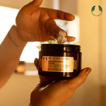 Hand applying cream from a jar labeled 'Spa of the World Hawaiian Kukui Cream' with a blurred background.