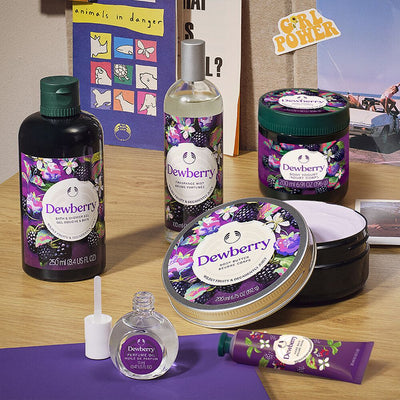 Collection of Dewberry beauty products on a wooden surface with a 'Girl Power' poster in the background.