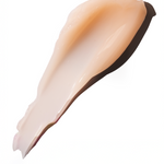 A thick, glossy smear of light peach-beige cream or gel makeup swatch on a solid white background.
