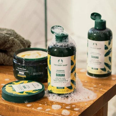 The Body Shop Banana shampoo and body scrub on a wooden surface with a neutral background