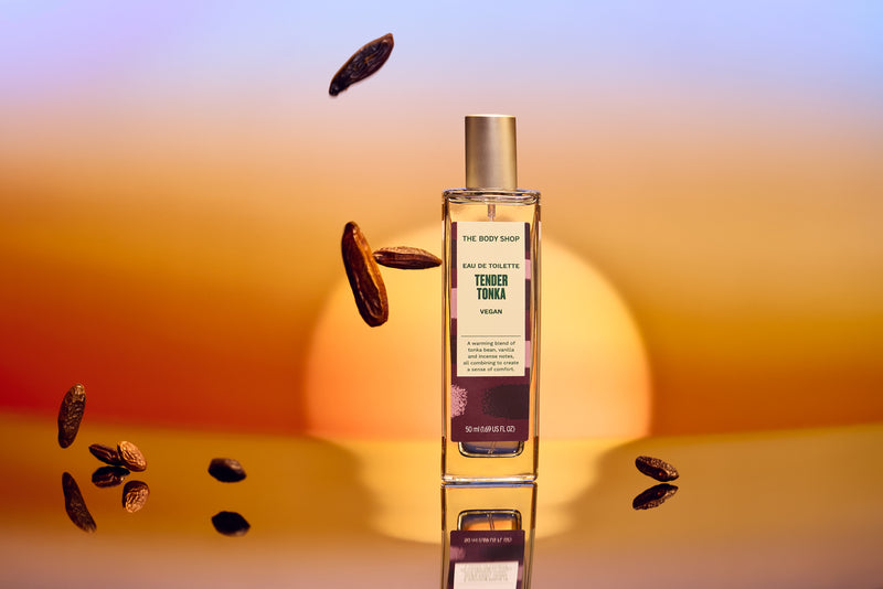 Bottle of 'The Body Shop' Tender Touch perfume with scattered almonds on a gradient background