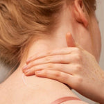 Close-up of a person's neck and shoulder with one hand gently touching the skin.