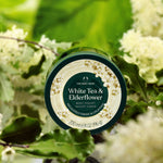 Body yogurt container labeled 'White Tea & Elderflower' by The Body Shop with green leaves and flowers in the background.