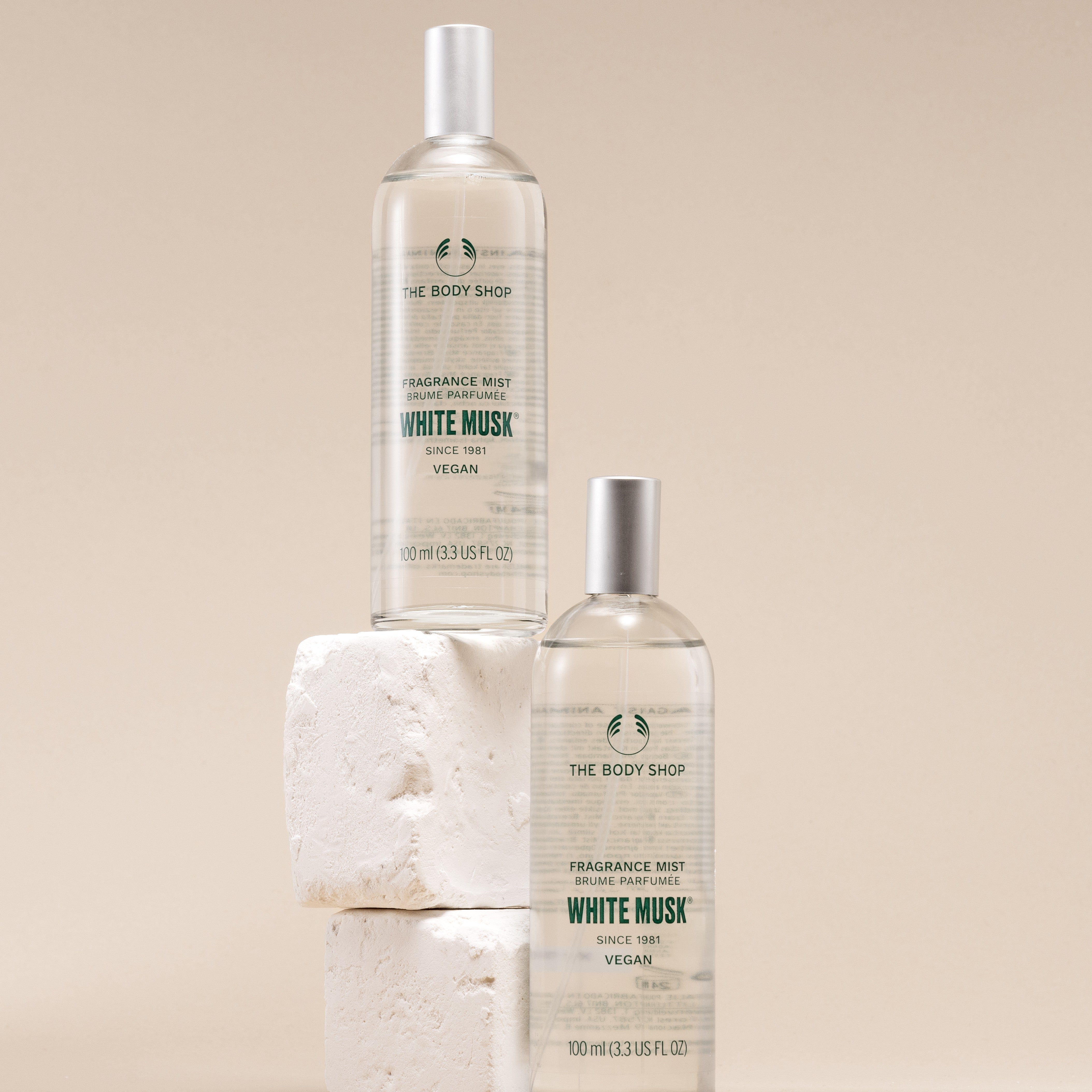 Two bottles of The Body Shop White Musk fragrance mist on a beige background