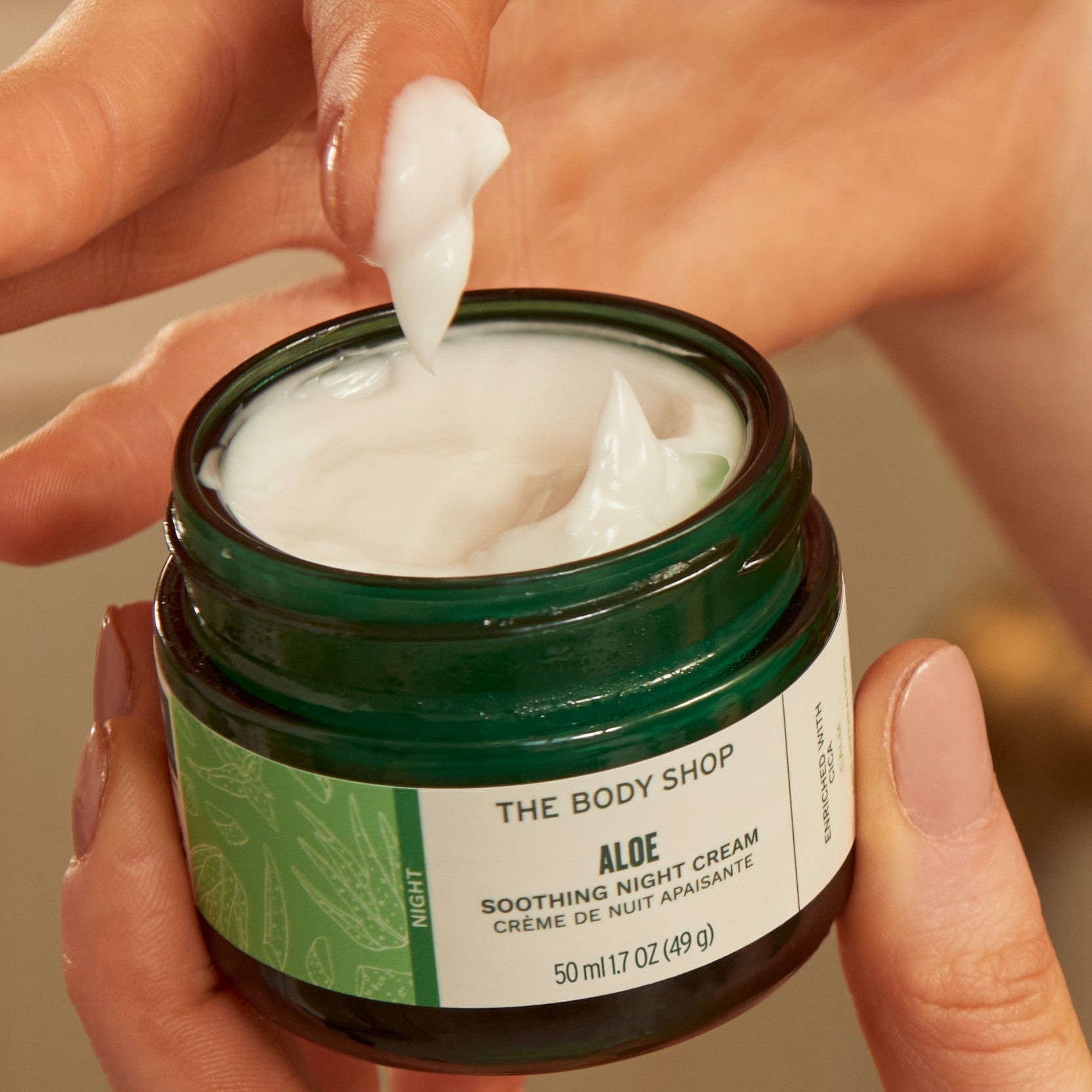 Person applying aloe vera cream to their hand with a jar of The Body Shop Aloe Soothing Night Cream.