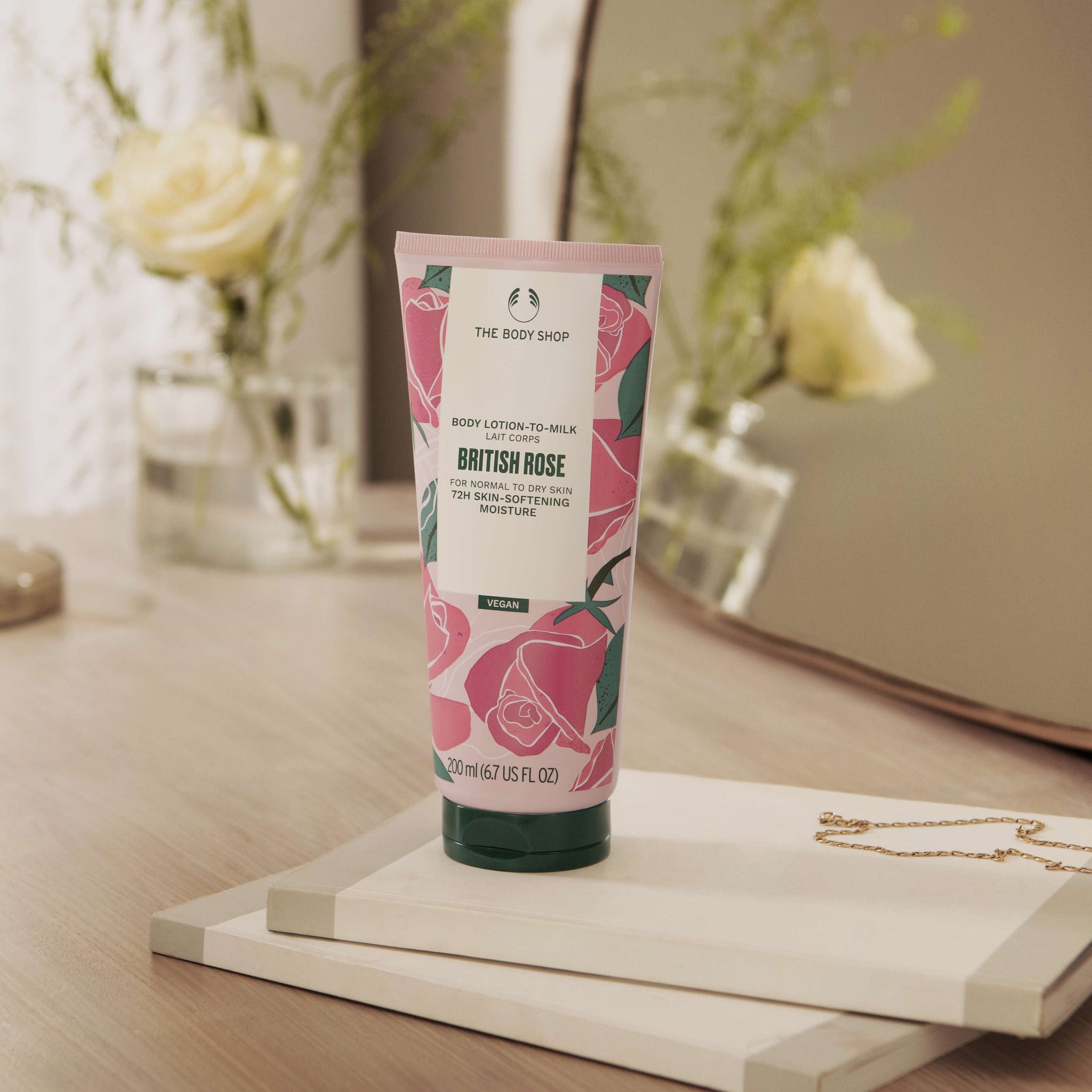 Tube of The Body Shop British Rose body lotion on a wooden surface with flowers in the background