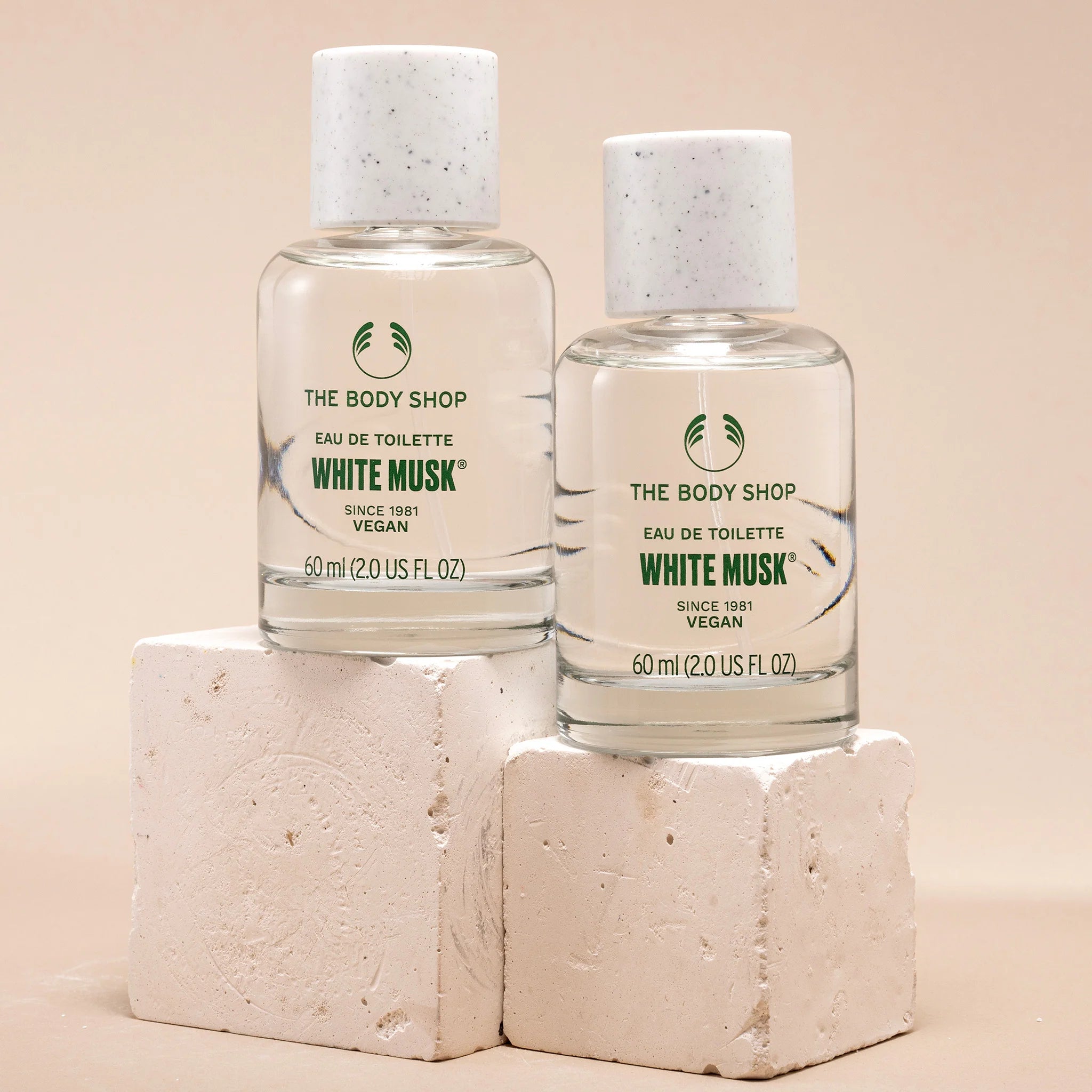 Two bottles of The Body Shop White Musk eau de toilette on beige blocks with a beige background.