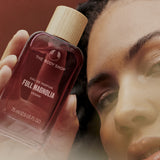 Person holding a 'The Body Shop' Full Magnolia perfume bottle close to their face.