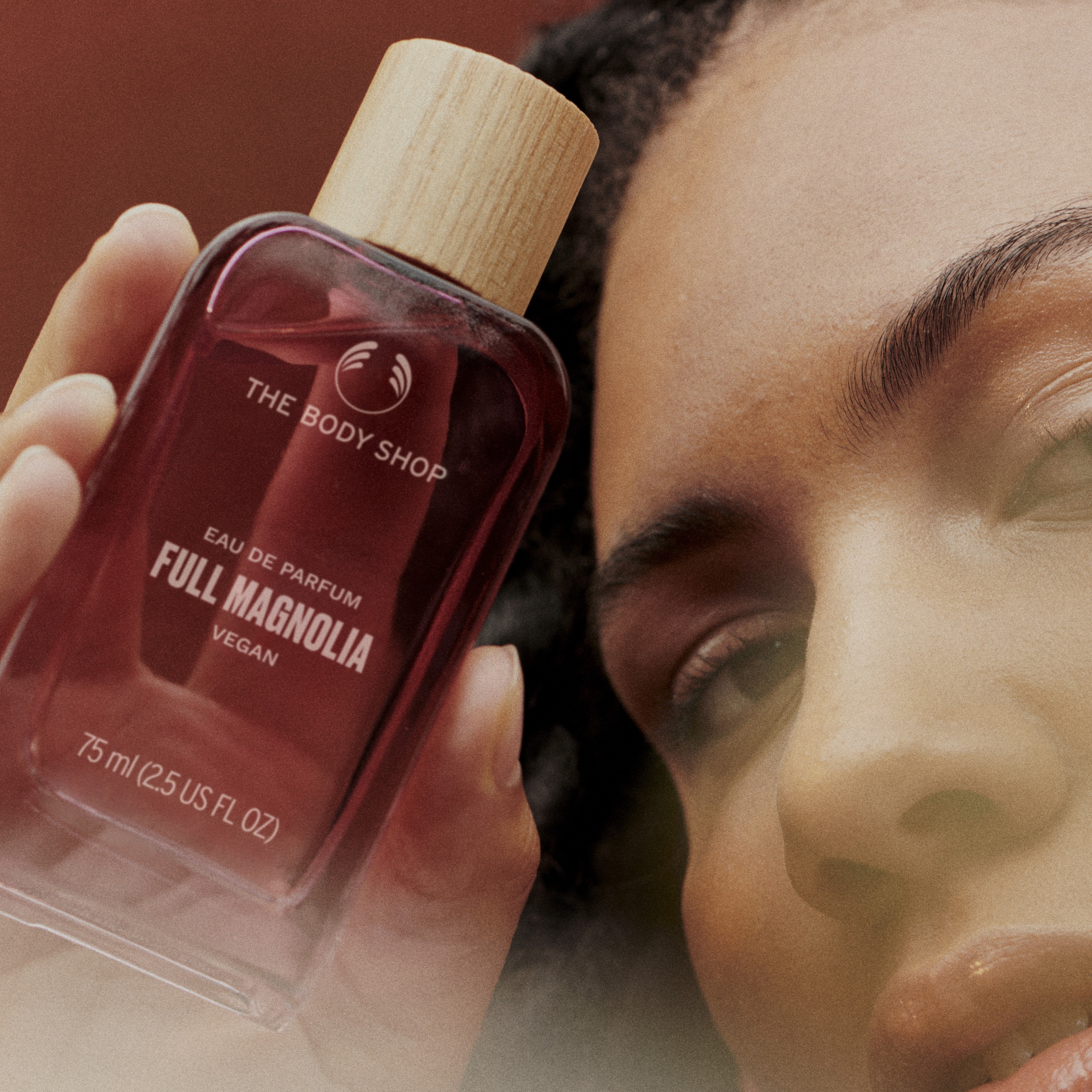 Person holding a 'The Body Shop' Full Magnolia perfume bottle close to their face.