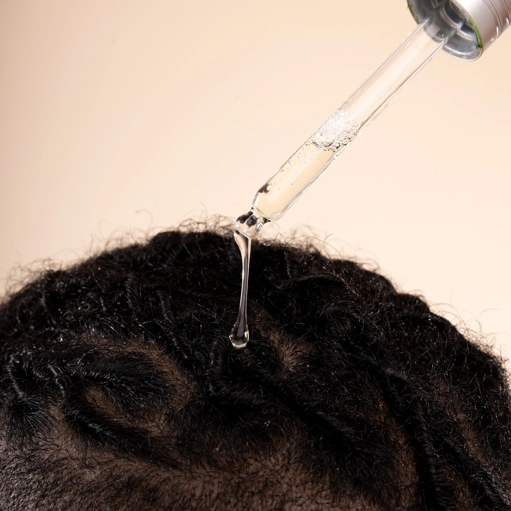 Bottle of hair oil being dripped onto braided hair against a beige background
