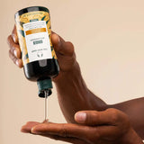 Hand holding a bottle of hair oil with visible brand label against a beige background