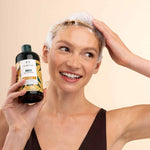 Woman with soapy hair holding a bottle of shampoo against a beige background