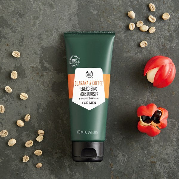 Tube of Guaraná & Coffee Energising Moisturiser for Men on a gray surface with coffee beans and red objects.