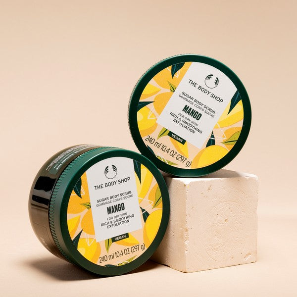 Two containers of The Body Shop Mango sugar body scrub on a beige background