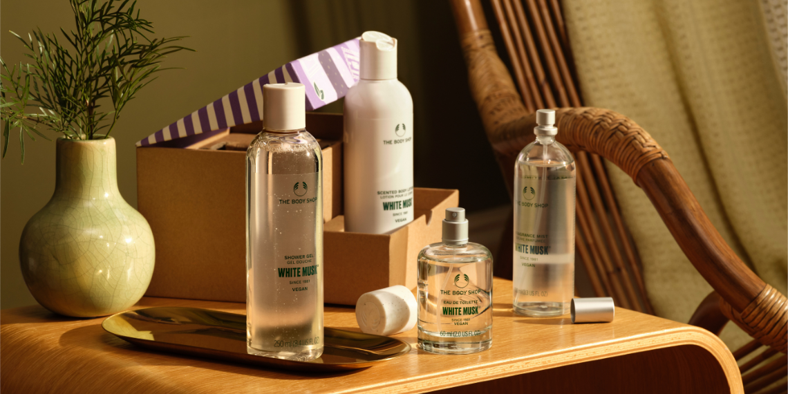 White Flower Fragrance bottles on a wooden table with a plant and box in the background.