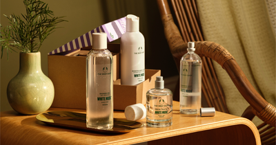 White Flower Fragrance bottles on a wooden table with a plant and box in the background.