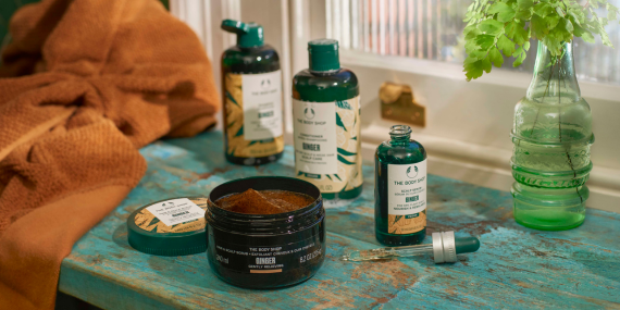 Cosmetic products on a textured surface with a vase of flowers and a towel.