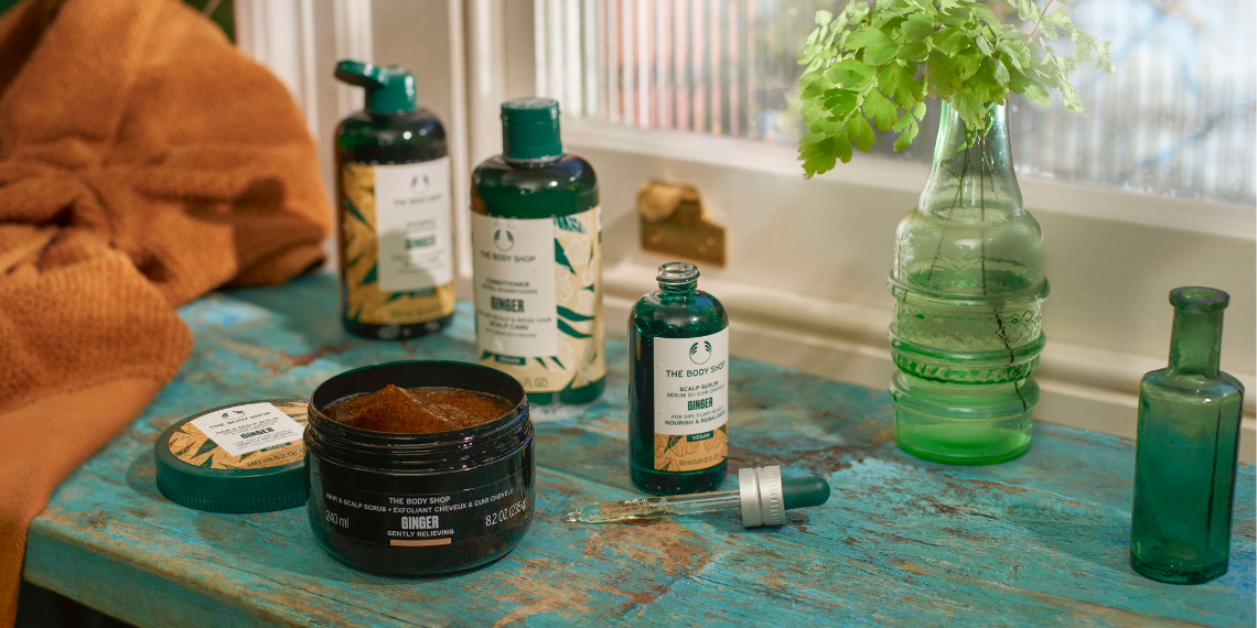 Cosmetic products on a textured surface with a vase of flowers and a towel.